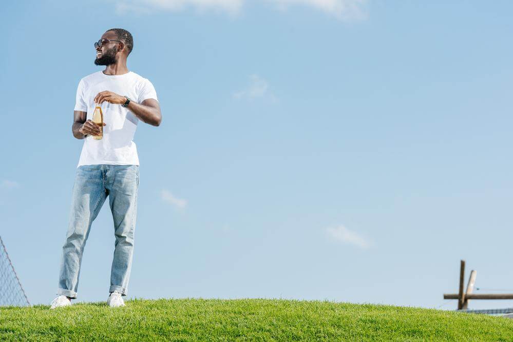 A guy is standing outside with a drink in hand.