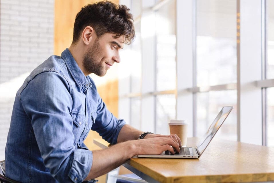 A guy is smiling while staring at his laptop.