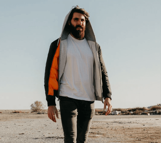 A bearded man wearing a hoodie and jeans in a desert seeking outpatient program for drug detox treatment.