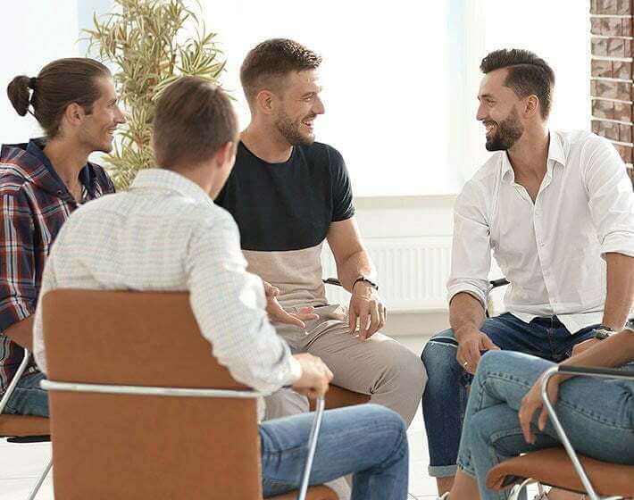 A group of men sitting around a table at an addiction recovery center, discussing their journey toward rehab and drug detox.