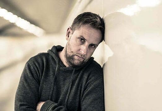 A man is leaning up against a wall, struggling from addiction to cocaine.