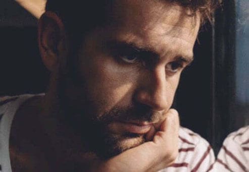 A man who looks to have a very dark expression is looking out the window.