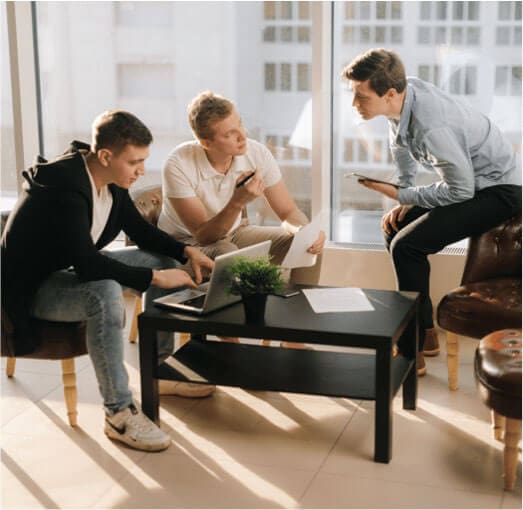Three guys are sitting around on a computer doing work.