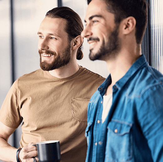 Two young men are talking while one is drinking coffee.