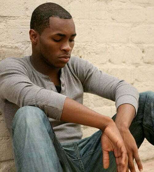 A young guy is sitting outside with his hands in his lap.