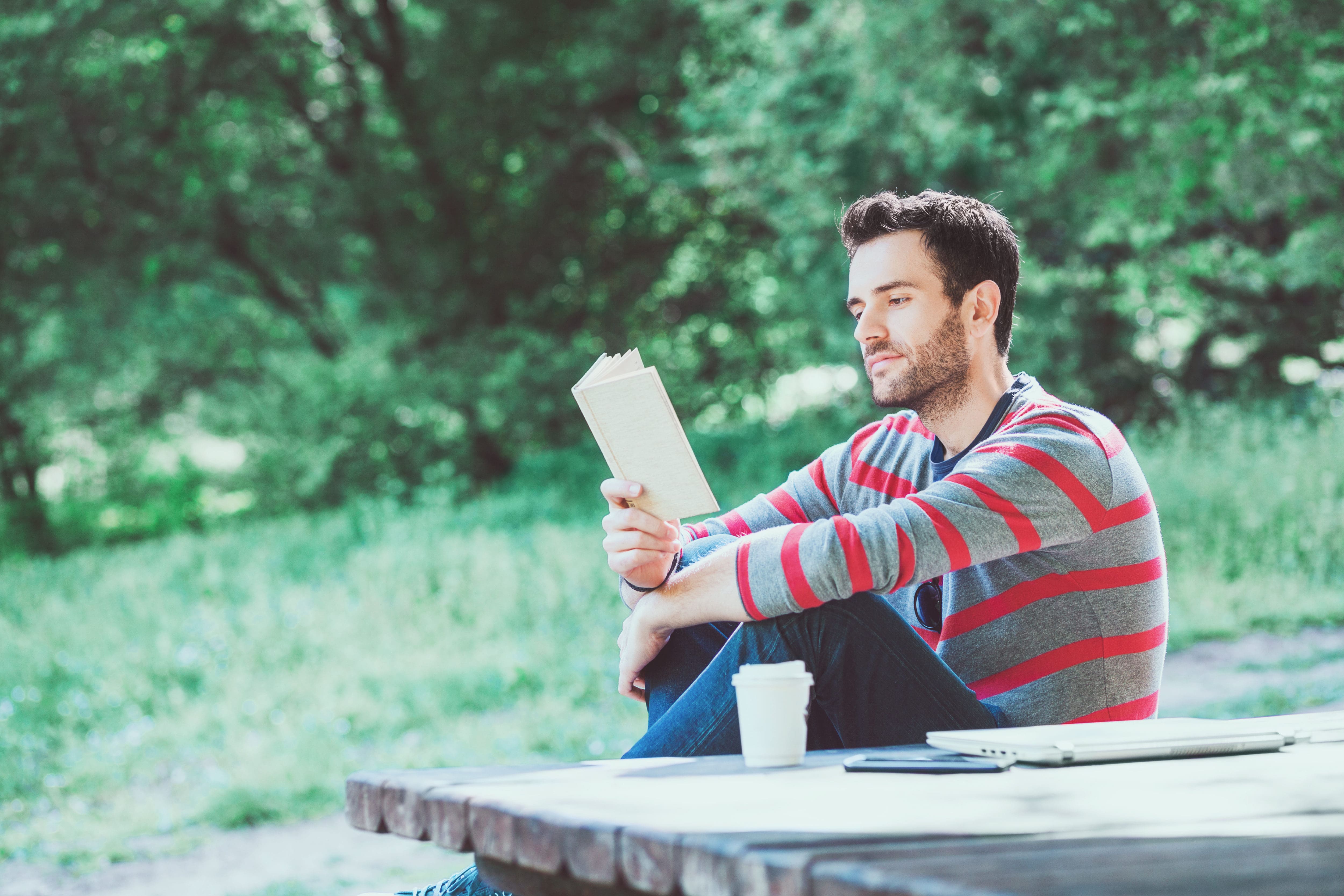 A man sitting on a picnic table enjoying a book at an inpatient treatment facility.