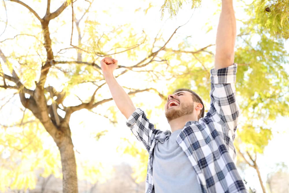A man in a park, raising his arms in the air with a sense of freedom and joy.
