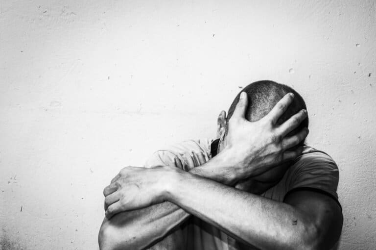 A black and white photo of a man in rehab, with his hands on his head.