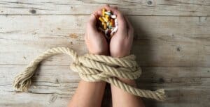 A woman's hands tied up with pills on a wooden table at an inpatient treatment facility.