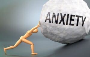 A man struggling with anxiety pushes a large rock, seeking relief through outpatient program or rehab treatment.